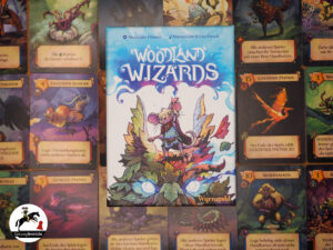 Kartenspiel Woodland Wizards ist mittig zu sehen. Im Hintergrund in Reihen und Spalten verschiedene Spielkarten aufgereiht.