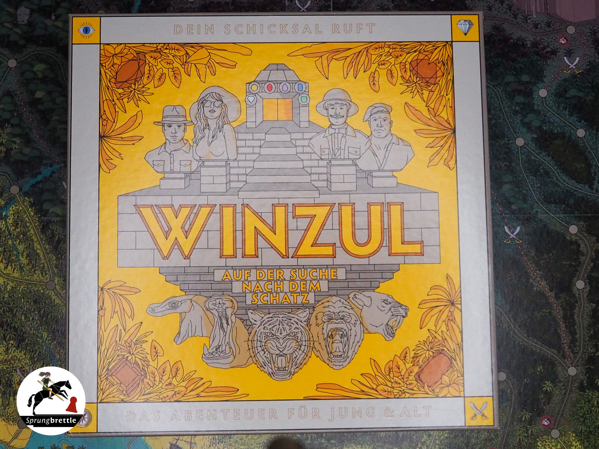 Winzul in der Tischmitte. Hauptsächlich gelbe Farben mit grauem Rand auf Spielfeld mit detailliert illustriertem Dschungel-Thema.
